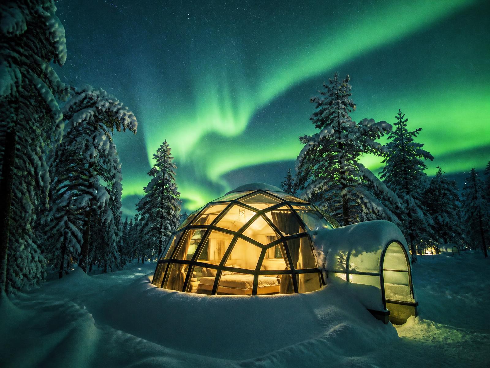 A glass-roofed igloo glowing beneath the green aurora in Arctic Norway